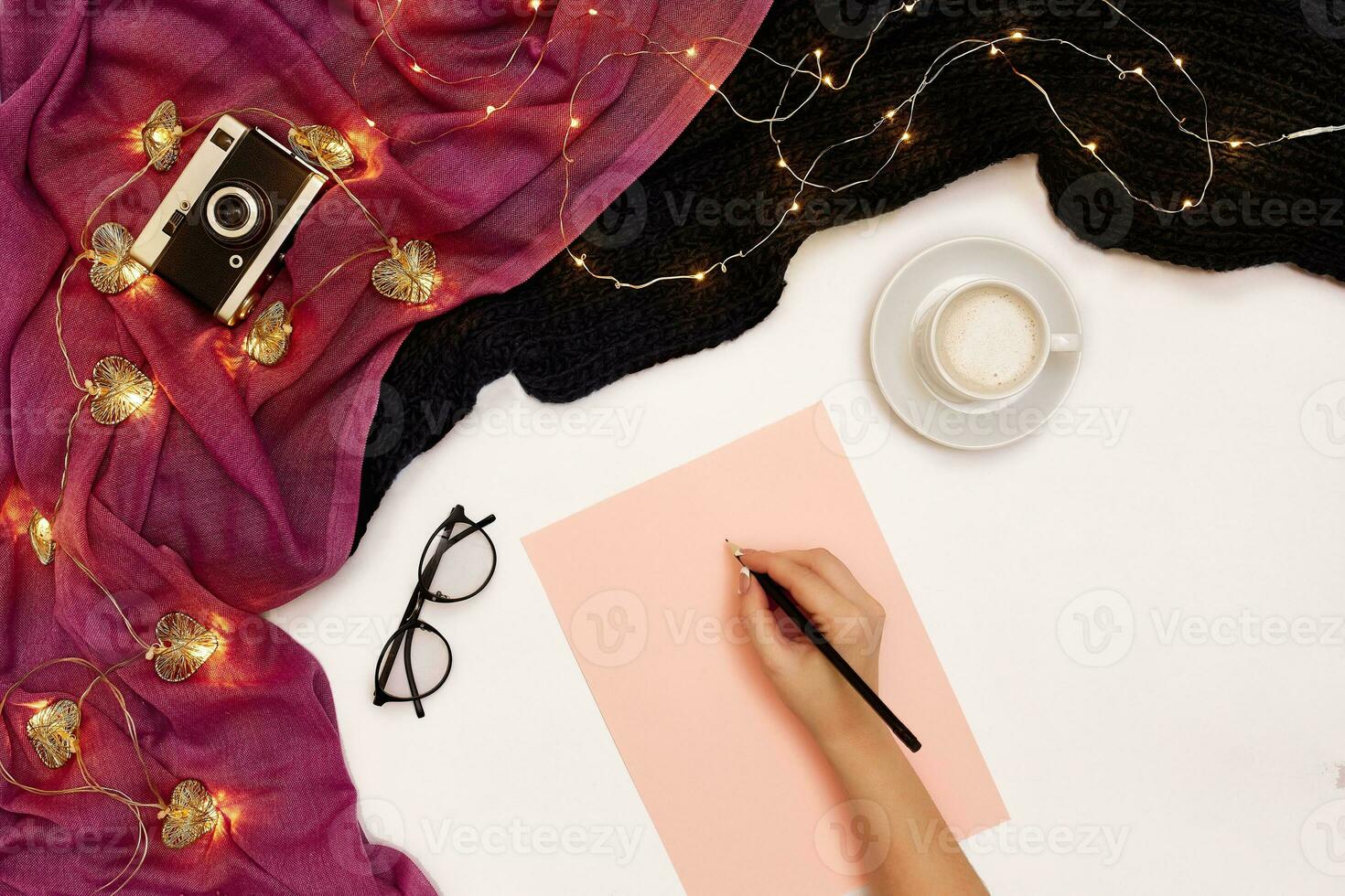 Top view of girl's hand writing in notepad placed on white surface with coffee cup and other items. Mock up photo