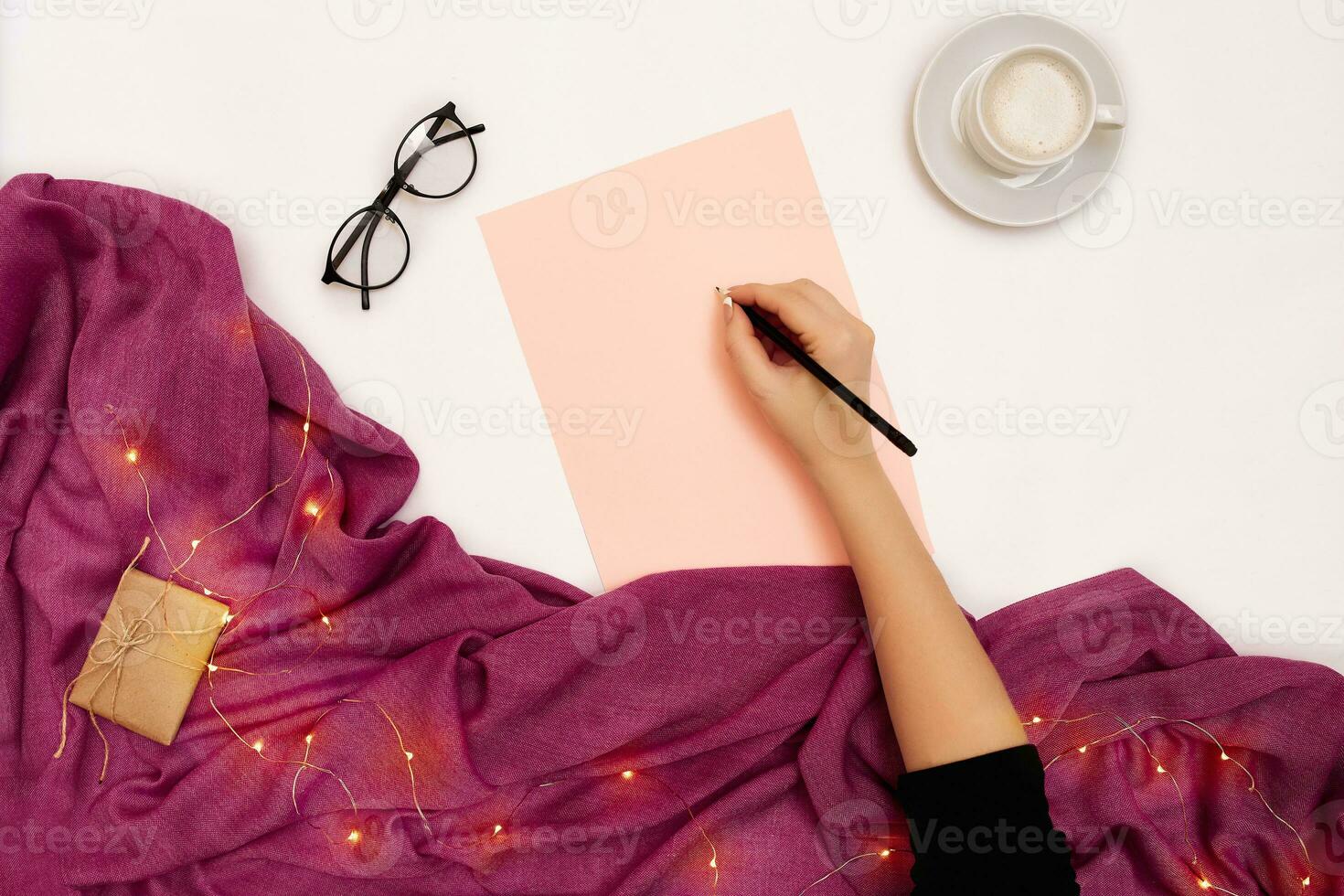 Top view of girl's hand writing in notepad placed on white surface with coffee cup and other items. Mock up photo