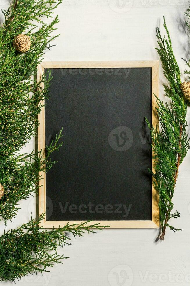 Juniper branches with a Christmas decor. Christmas, New Year background. Coniferous branches of juniper and black writing board. Top view, flat design. photo