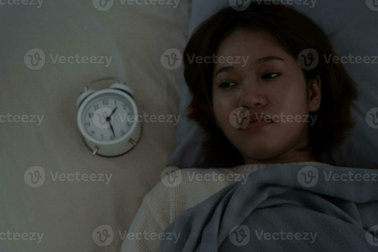 asian woman in bed late trying to sleep suffering insomnia, sleepless or scared in a nightmare, looking sad worried and stressed. Tired and headache or migraine waking up in the middle of the night. photo