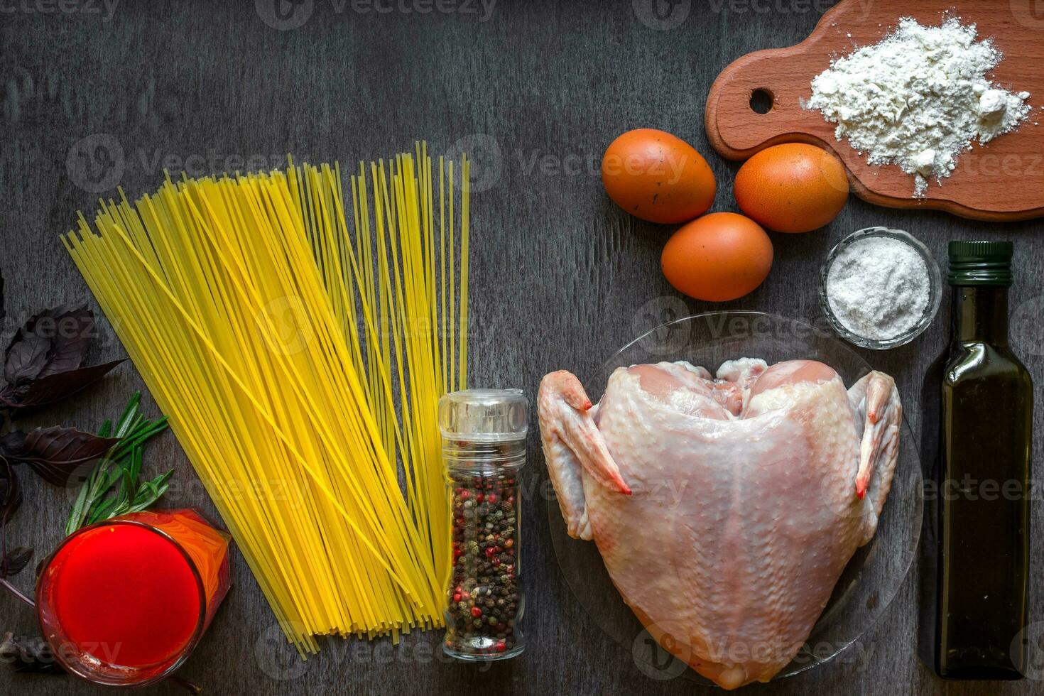 Cooked spaghetti noodles. Uncooked spaghetti and raw chicken on board. Ingredients for home-made noodles chicken eggs, vegetable oil. The dark black wood background. Top view. photo