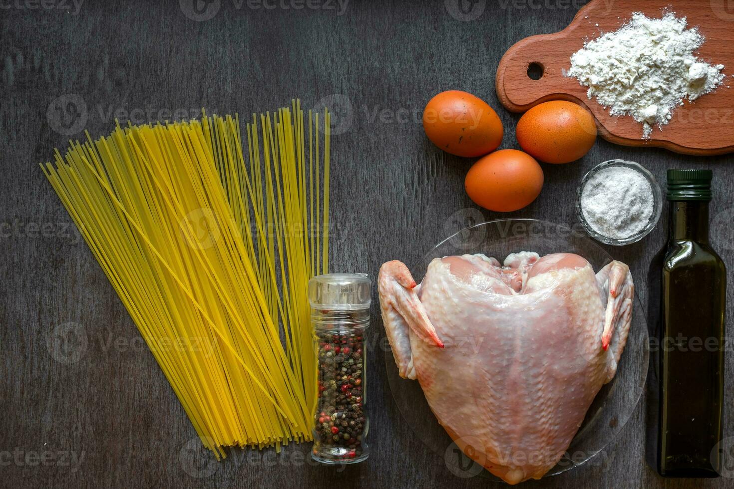 Cooked spaghetti noodles. Uncooked spaghetti and raw chicken on board. Ingredients for home-made noodles chicken eggs, vegetable oil. The dark black wood background. Top view. photo