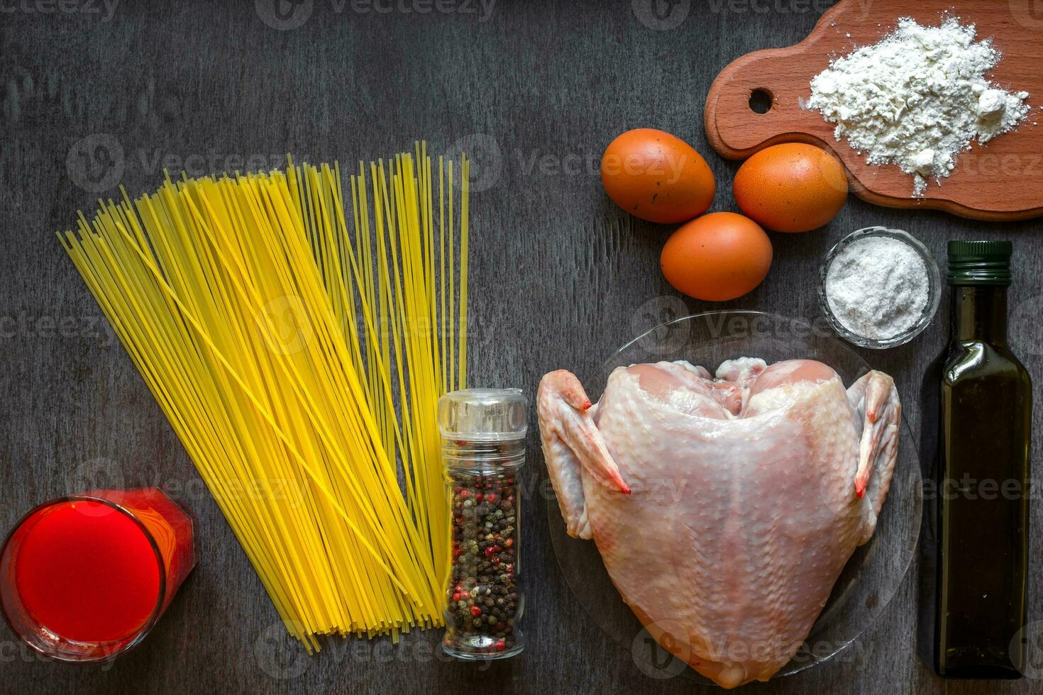 Cooked spaghetti noodles. Uncooked spaghetti and raw chicken on board. Ingredients for home-made noodles chicken eggs, vegetable oil. The dark black wood background. Top view. photo