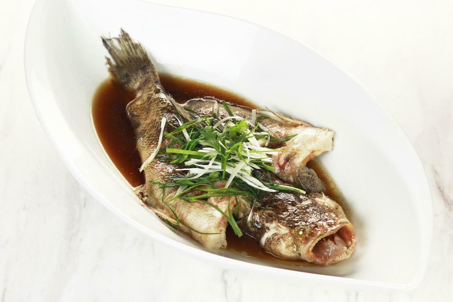 steam fried Marbled Goby fish called Ikan Malas in siamese style served in a dish on a wooden table in a restaurant in Indonesia photo