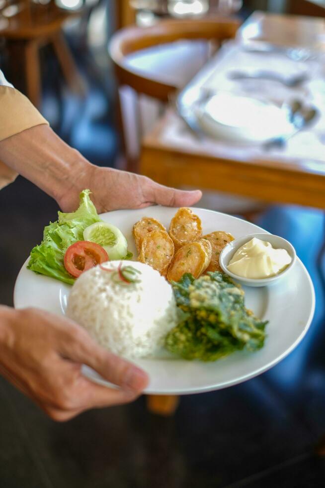 camareros en Indonesia llevar blanco platos conteniendo el comida ese será ser servido. el comida consiste de verduras, carne y mayonesa foto