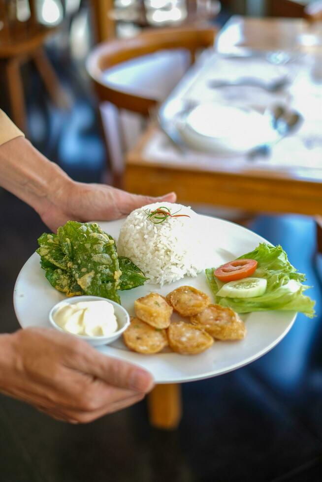 camareros en Indonesia llevar blanco platos conteniendo el comida ese será ser servido. el comida consiste de verduras, carne y mayonesa foto