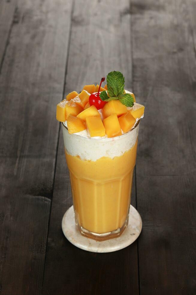 yellow mango juice with garnish of mango pieces, cherries and mint leaves. with a white background and dark wood photo