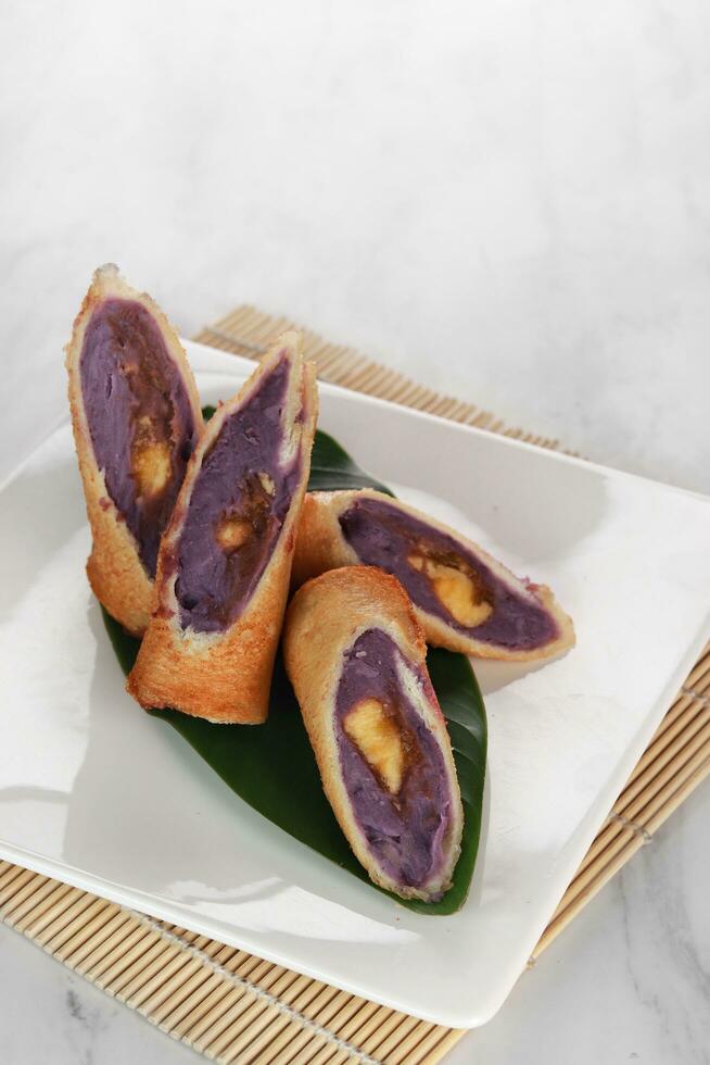 roll purple sweet potato cakes served on a wooden and leaf base with a white background photo