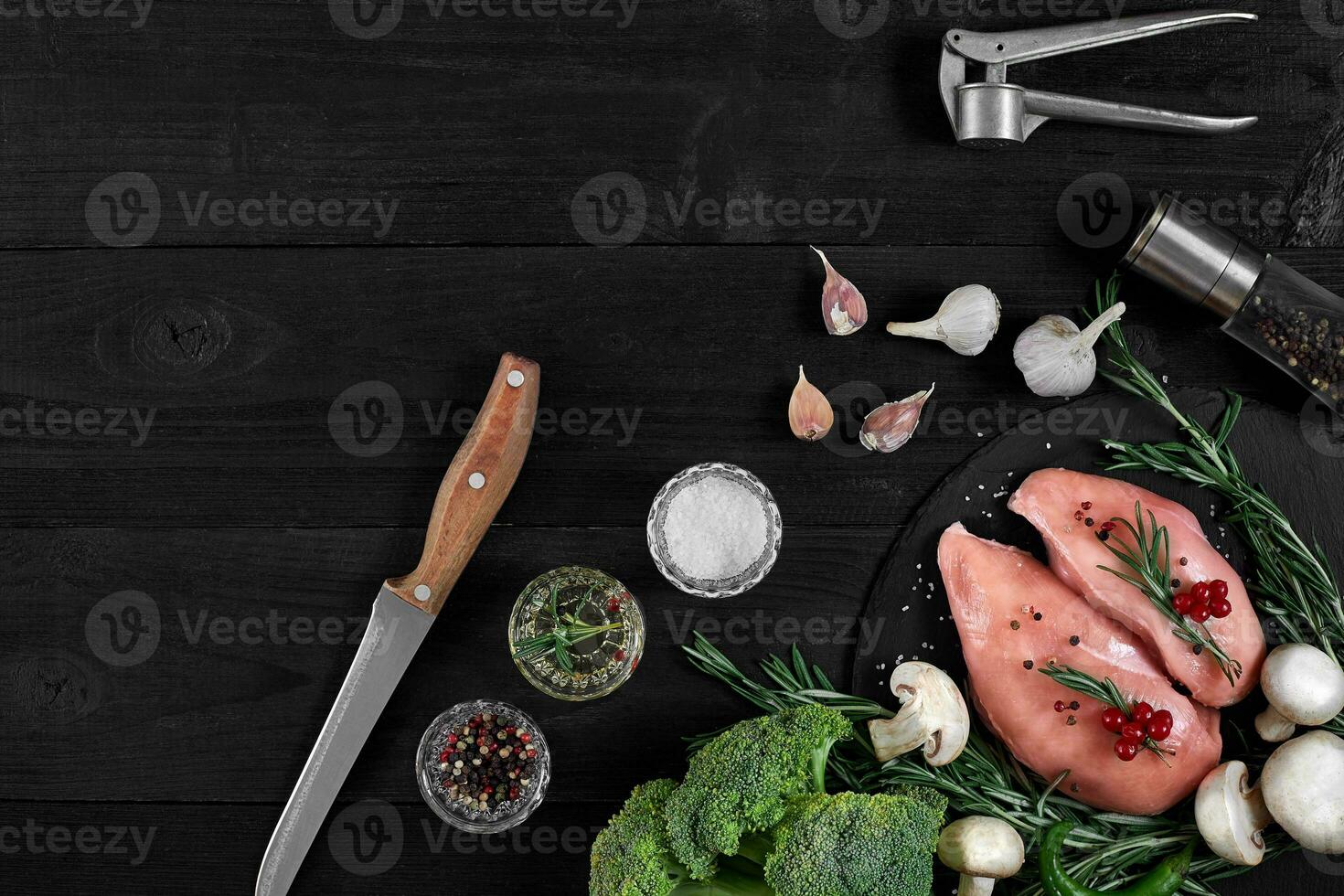 Chicken breast on a cutting board with herbs and different vegetables on rustic wooden background. photo