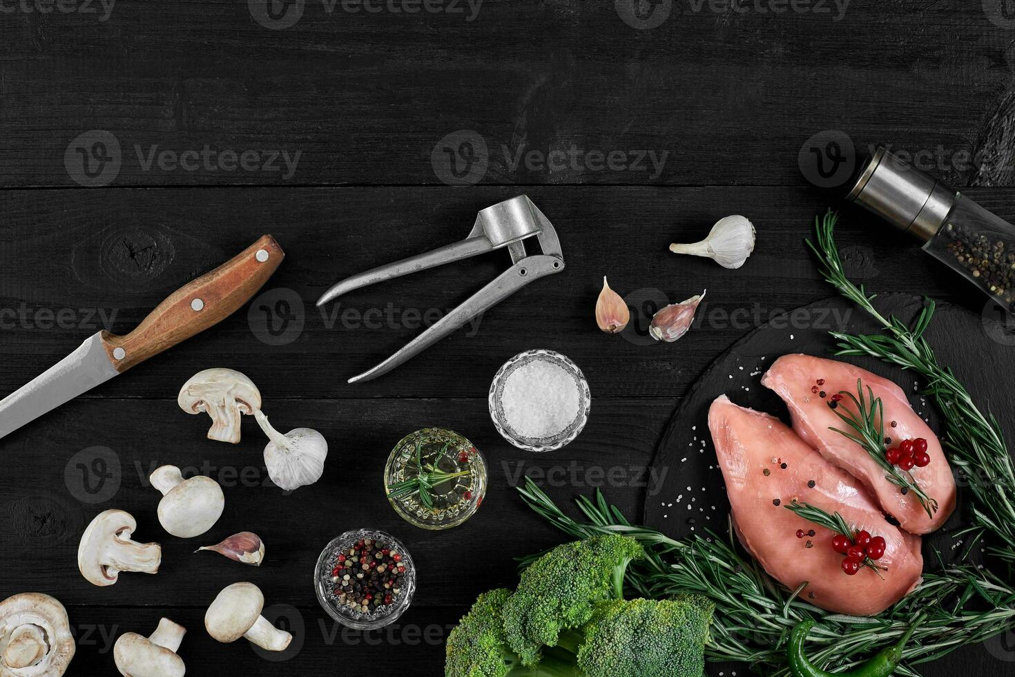 Chicken breast on a cutting board with herbs and different vegetables on rustic wooden background. photo