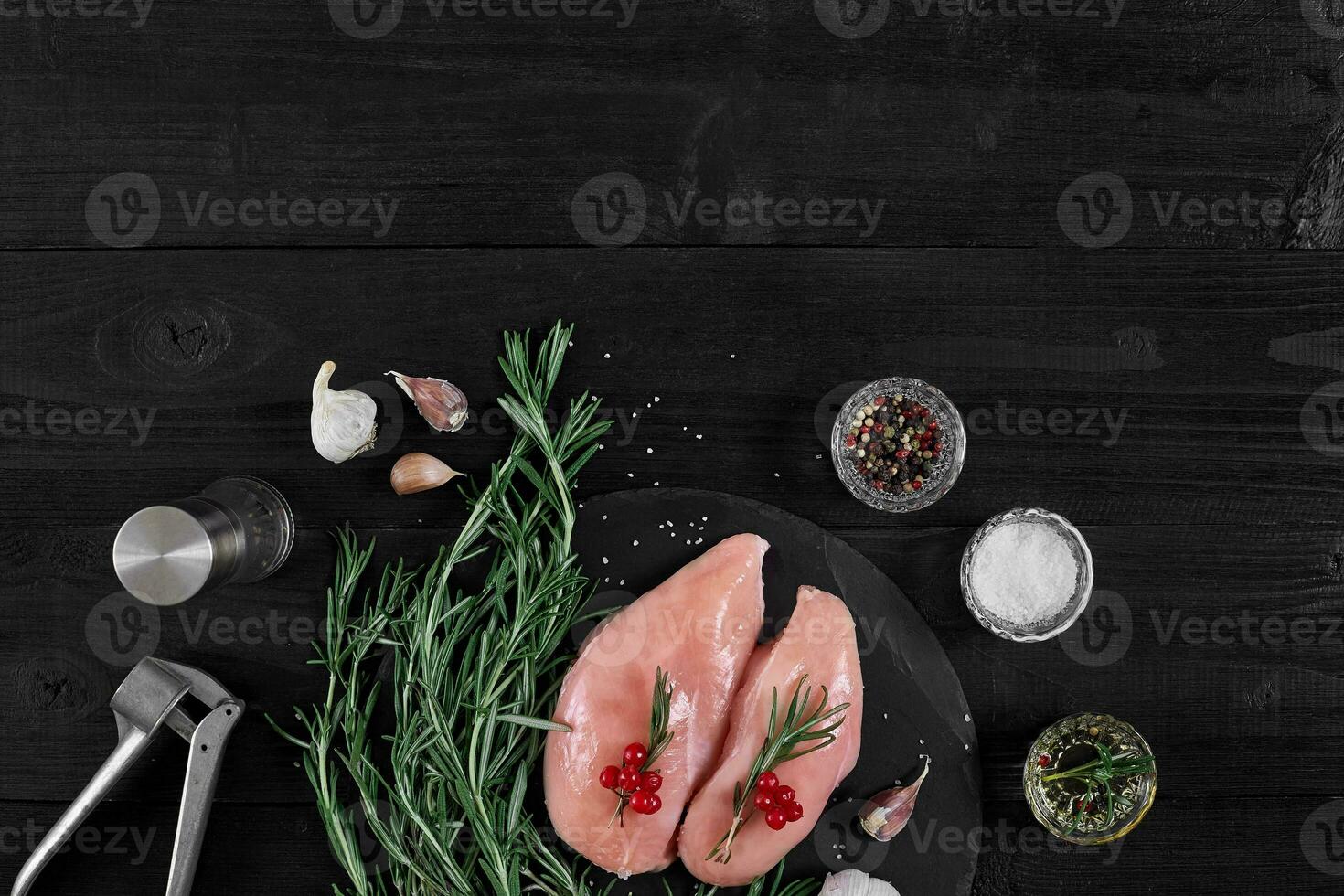 Chicken breast on a cutting board with herbs, spices and garlic press on rustic wooden background. photo