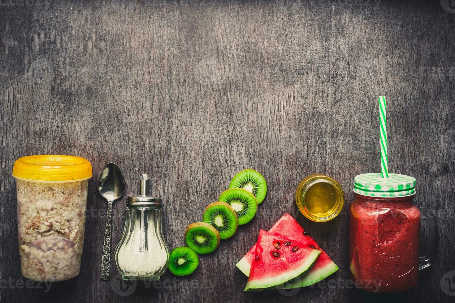 Healthy breakfast fresh smoothie in glass jar with oatmeal granola, kiwi and watermelon on dark wooden background. Toned photo