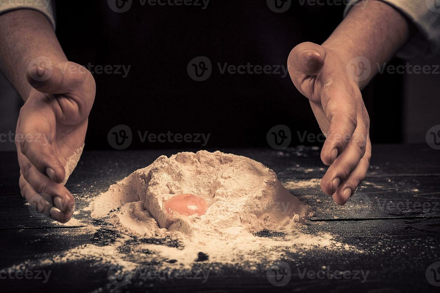 The chef breaks eggs into a flour on a wooden table photo