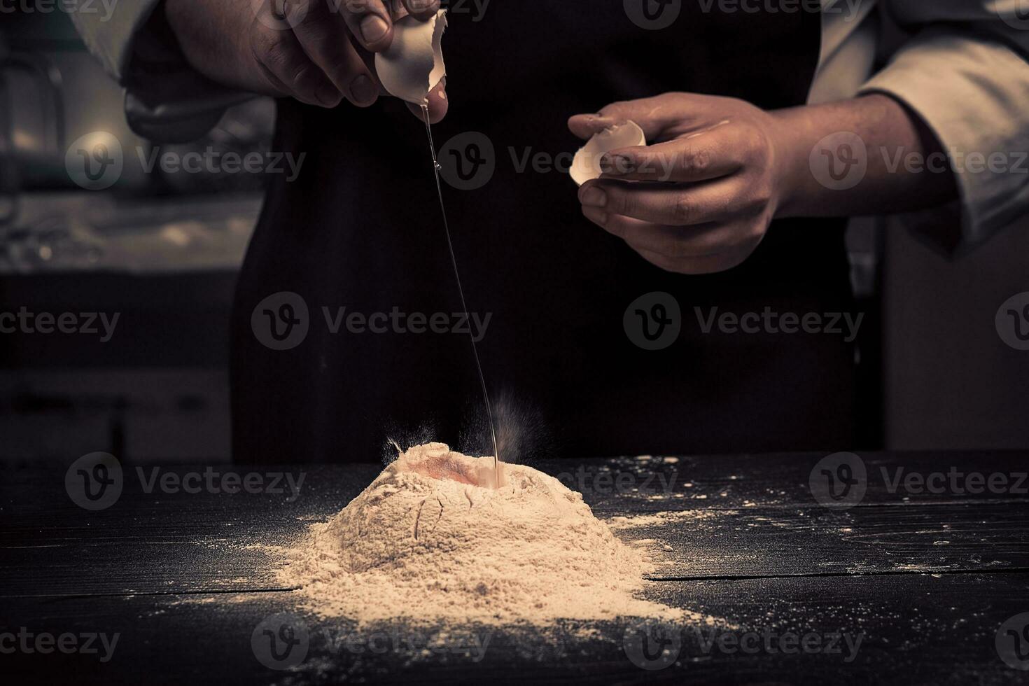 The chef breaks eggs into a flour on a wooden table photo