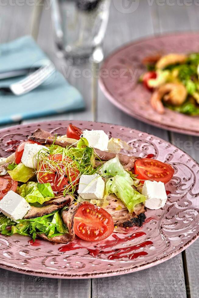 Healthy mixed Greek salad served on a pink plate with silver fork containing crisp leafy greens, microgreen, feta, onion, tomato and sliced beef photo
