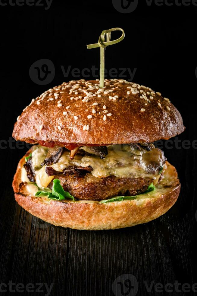 Cheese burger with grilled meat, cheese, tomato on dark wooden surface. Ideal for advertisement. Close-up photo