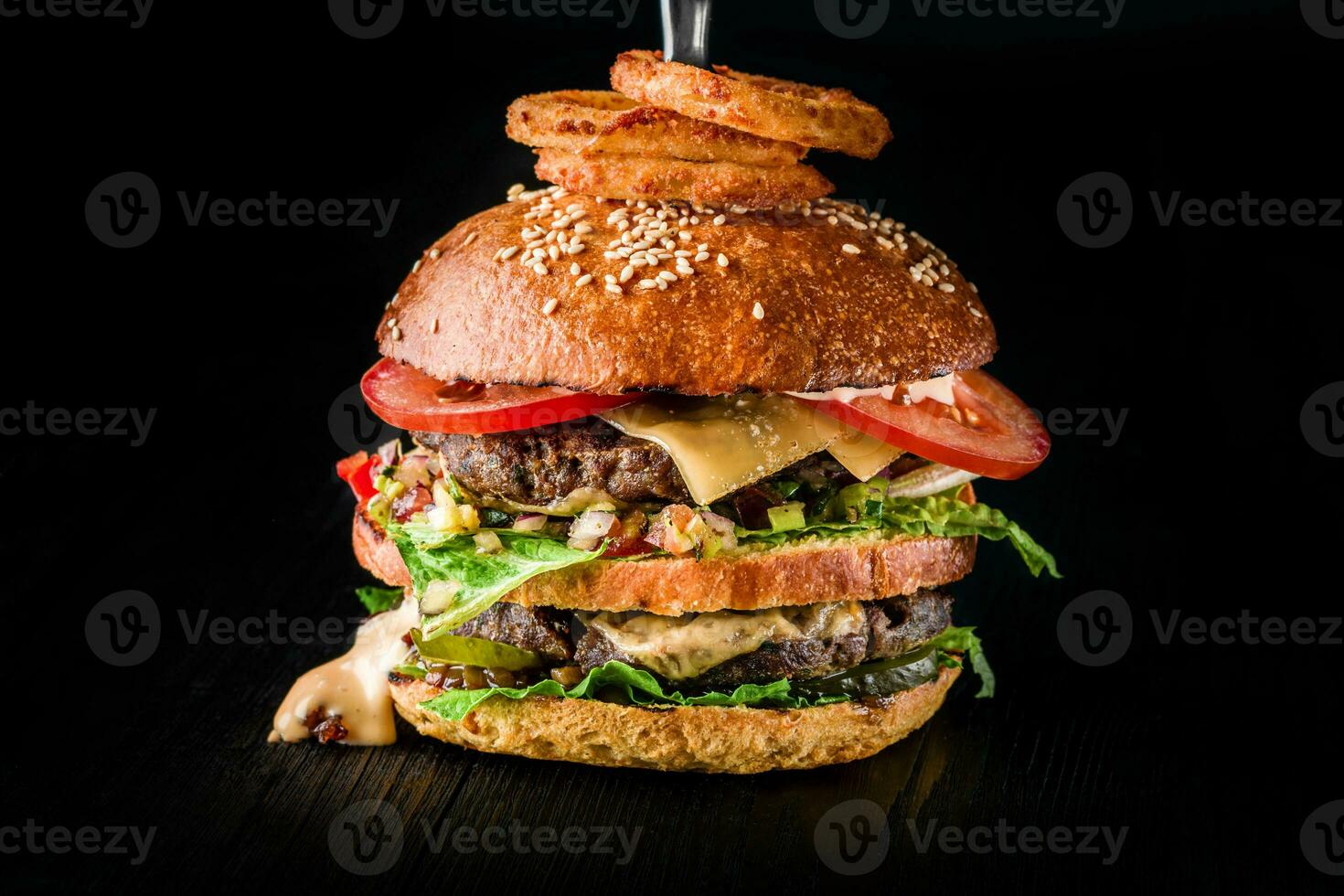Cheese burger with grilled meat, cheese, tomato and with onion rings on dark wooden surface. Ideal for advertisement. Close-up photo