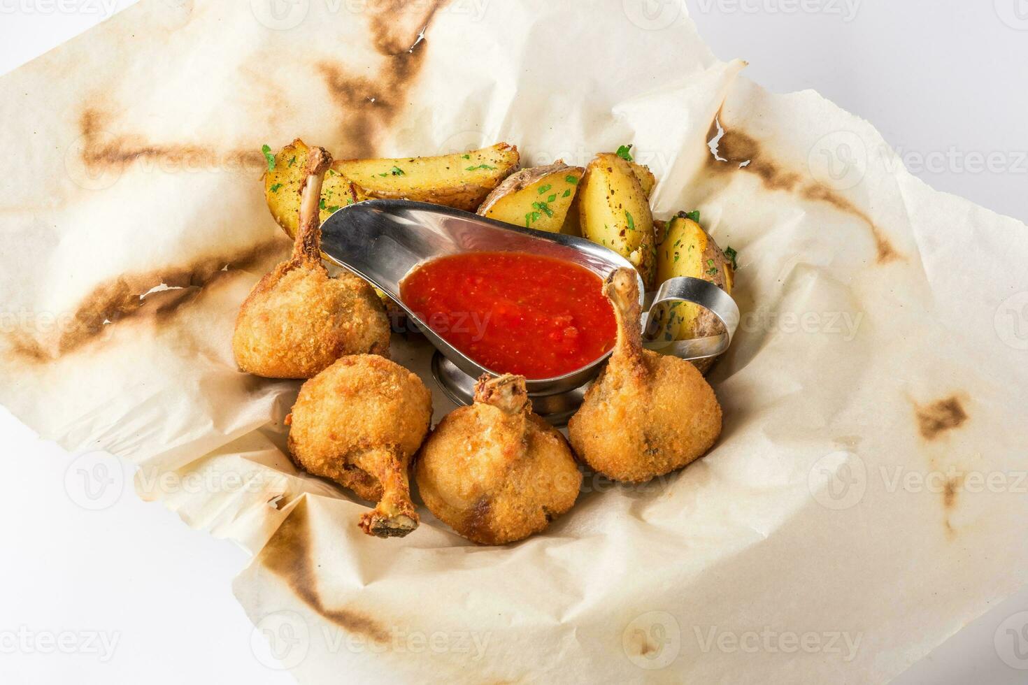 Fried chicken legs breaded and potato with sauce on a sheet of parchment photo