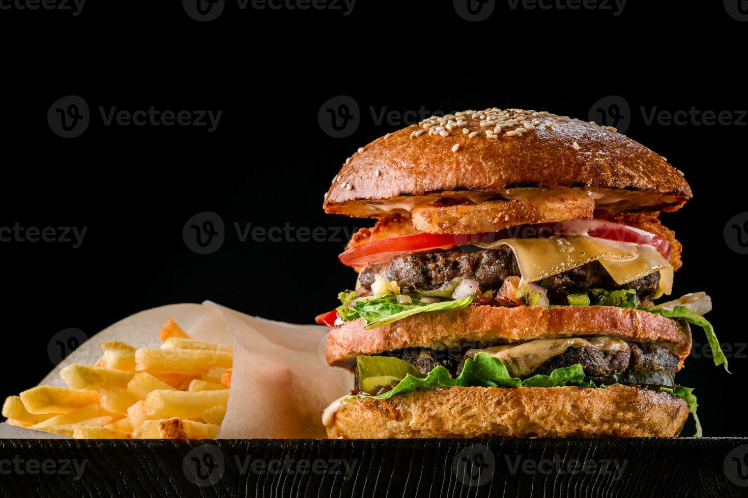 Cheese burger with grilled meat, cheese, tomato and potatoes on dark wooden surface. Ideal for advertisement. Close-up photo