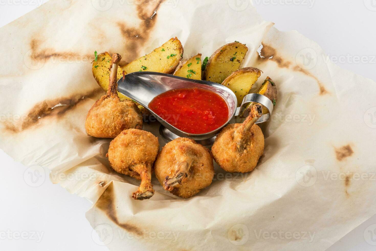 Fried chicken legs breaded and potato with sauce on a sheet of parchment photo