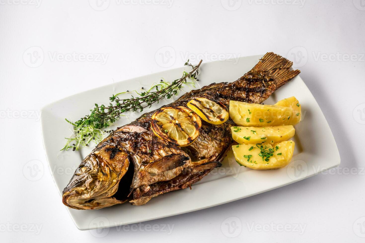 Grilled carp fish with rosemary potatoes and lemon, close up photo