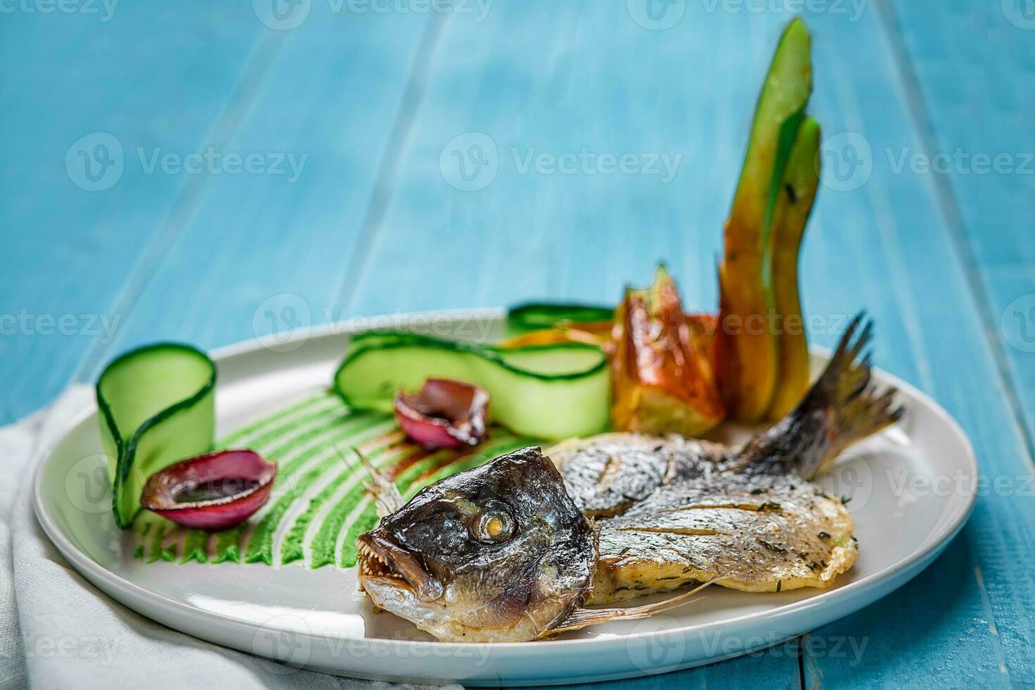 Fried fish dorado, decorated with cucumbers and onions. On a blue wooden background photo