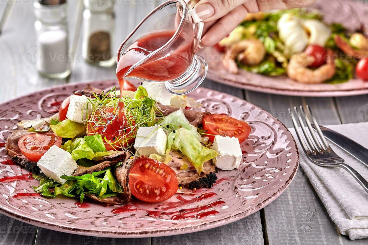 Healthy mixed Greek salad served on a pink plate with silver fork containing crisp leafy greens, microgreen, feta, onion, tomato and sliced beef photo