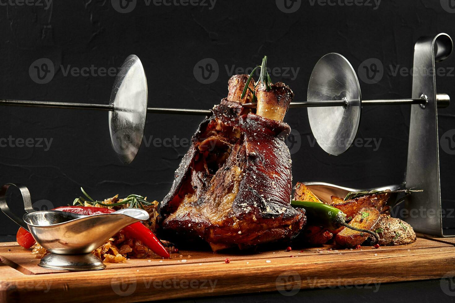 Roasted pork knuckle eisbein with braised boiled cabbage, potatoes, chili peppers and mustard on wooden cutting board, on a black background photo