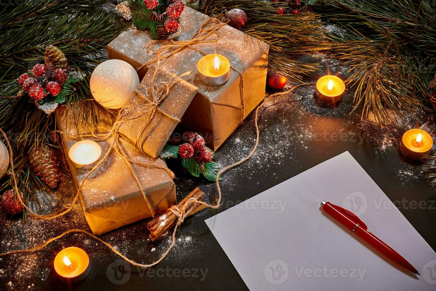 Christmas gifts, burning candles and notebook lying near green spruce branch on black background top view. Space for text photo