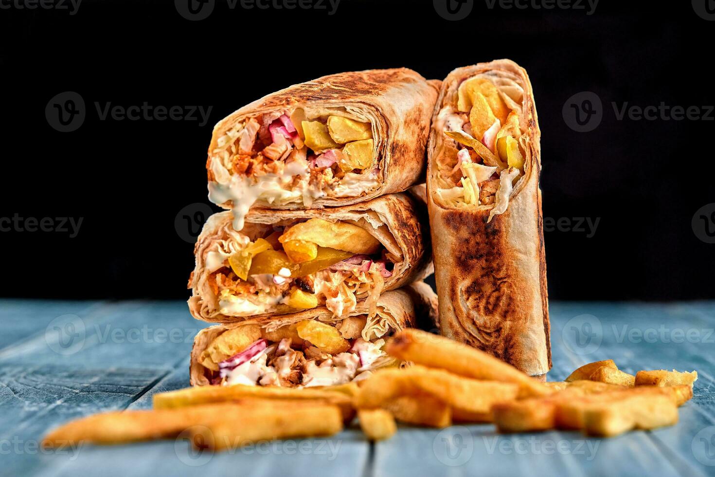 Shawarma chicken roll in a pita with fresh vegetables, cream sauce and french fries on wooden background. Selective focus photo