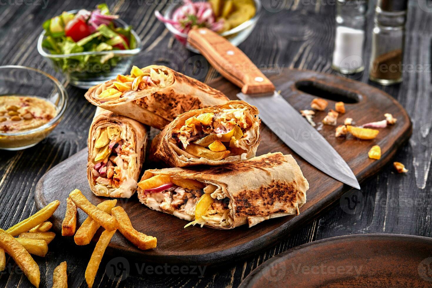 Shawarma chicken roll in a pita with fresh vegetables, cream sauce and french fries on wooden background. Selective focus photo