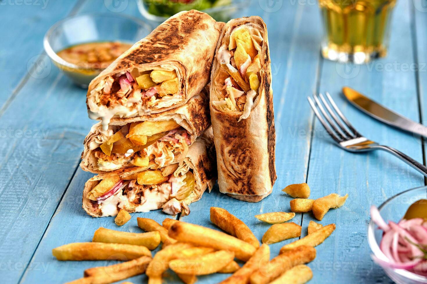 Shawarma chicken roll in a pita with fresh vegetables, cream sauce and french fries on wooden background. Selective focus photo