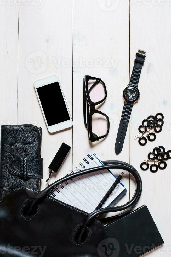 Women's accessories fell out of the black handbag on white background. photo