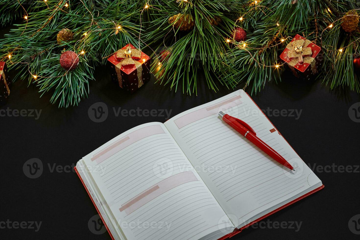 Christmas toys and notebook lying near green spruce branch on black background top view. Space for text photo
