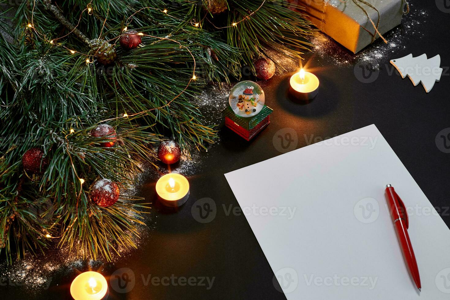 Red Christmas balls and notebook lying near green spruce branch on black background top view. Space for text photo