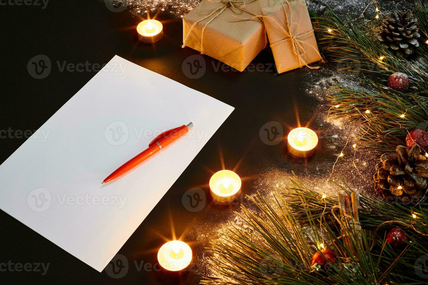 Christmas toys, burning candles and notebook lying near green spruce branch on black background top view. Space for text photo