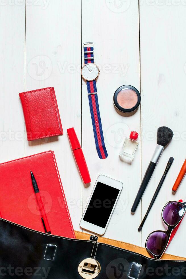 Cosmetics and women's accessories fell out of the black handbag on white background. photo