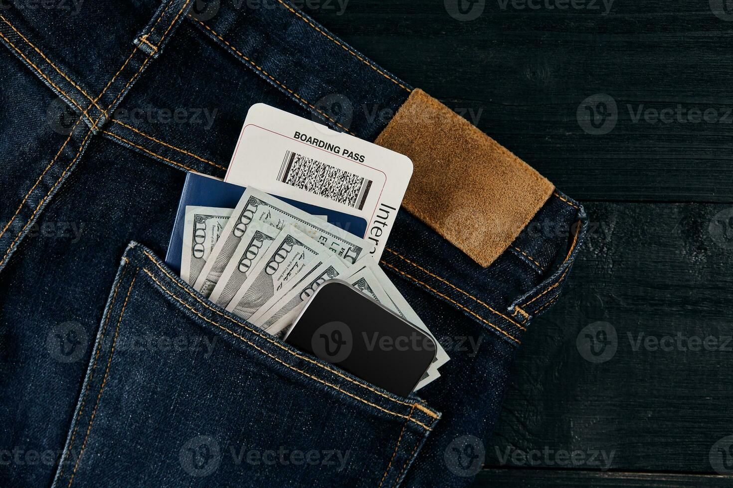 Dollars, smart, passport and plane ticket in your pocket jeans on black wooden background photo