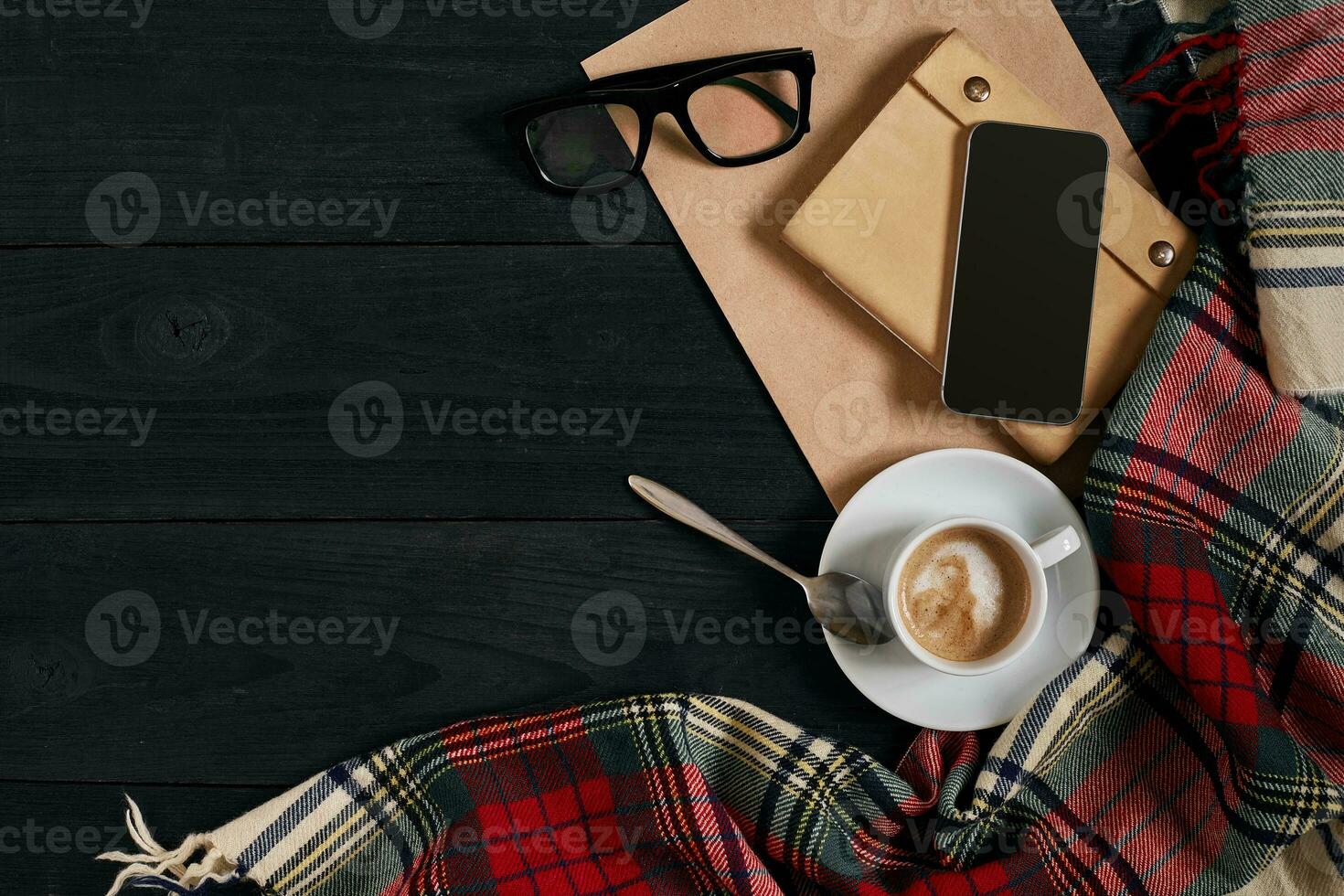 Above view of Smart phone with notebook and cup of latte coffee on black wooden background. photo