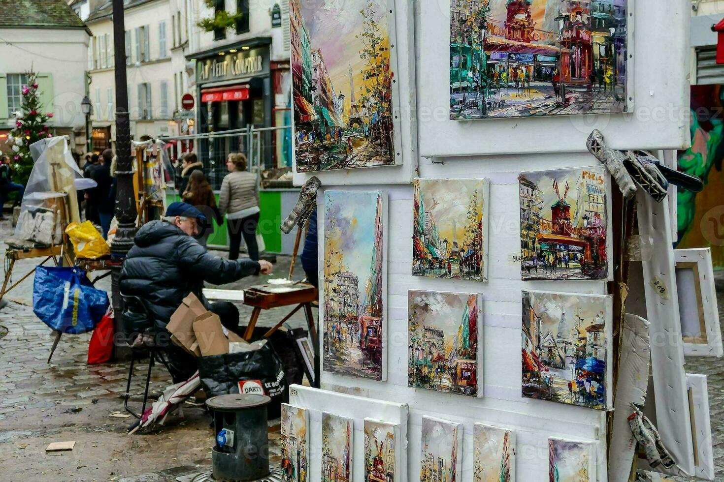 a man is painting on a street corner in front of paintings photo