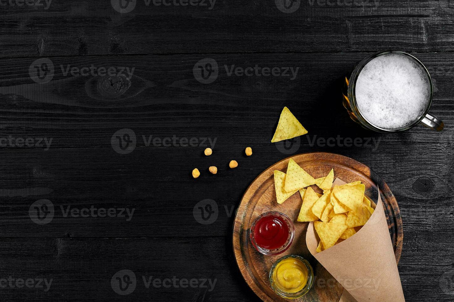 Top view of tortilla chips with sauce, glass of beer on black wooden background photo