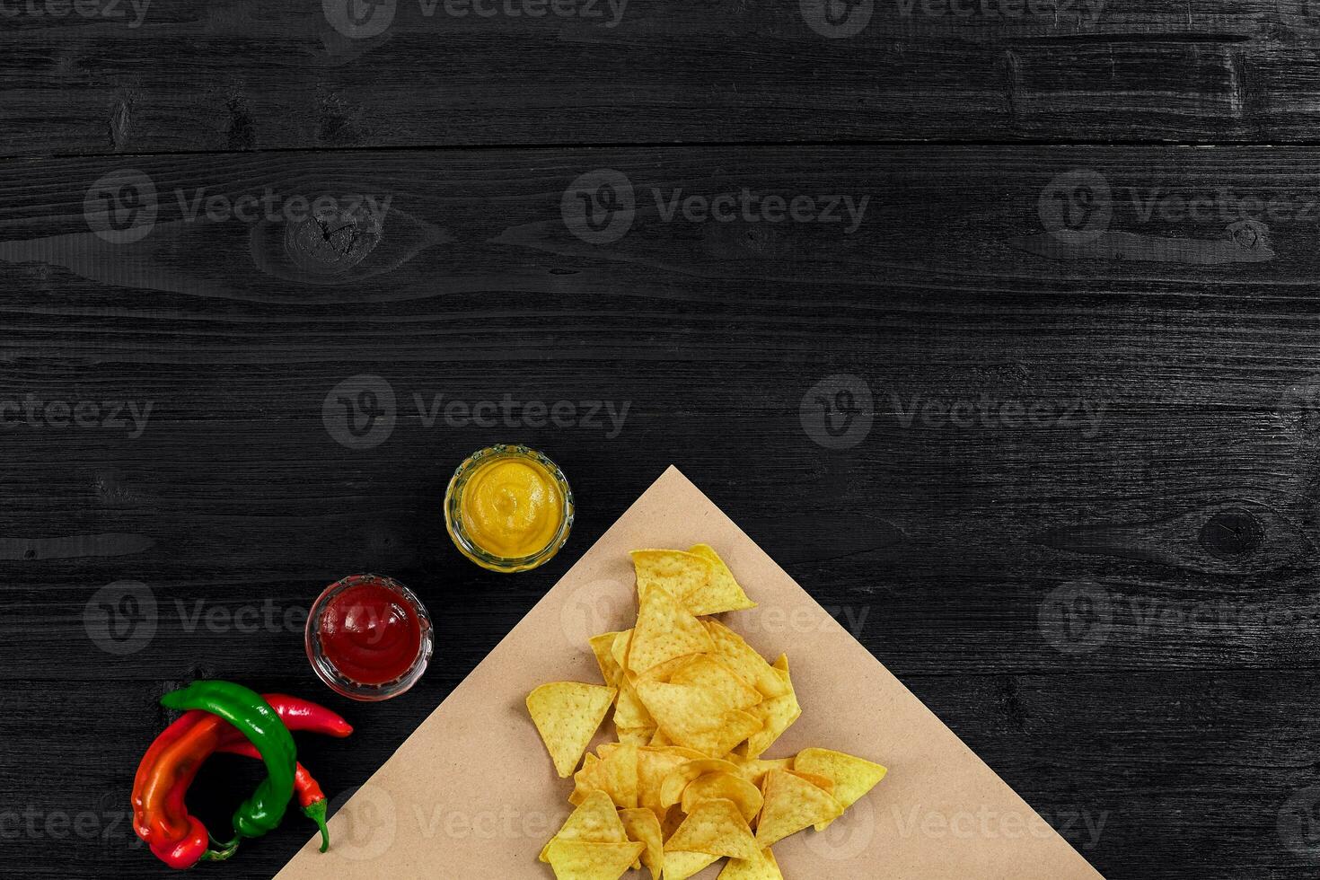 Top view of tortilla chips with sauce and red chili pepper on black wooden background photo