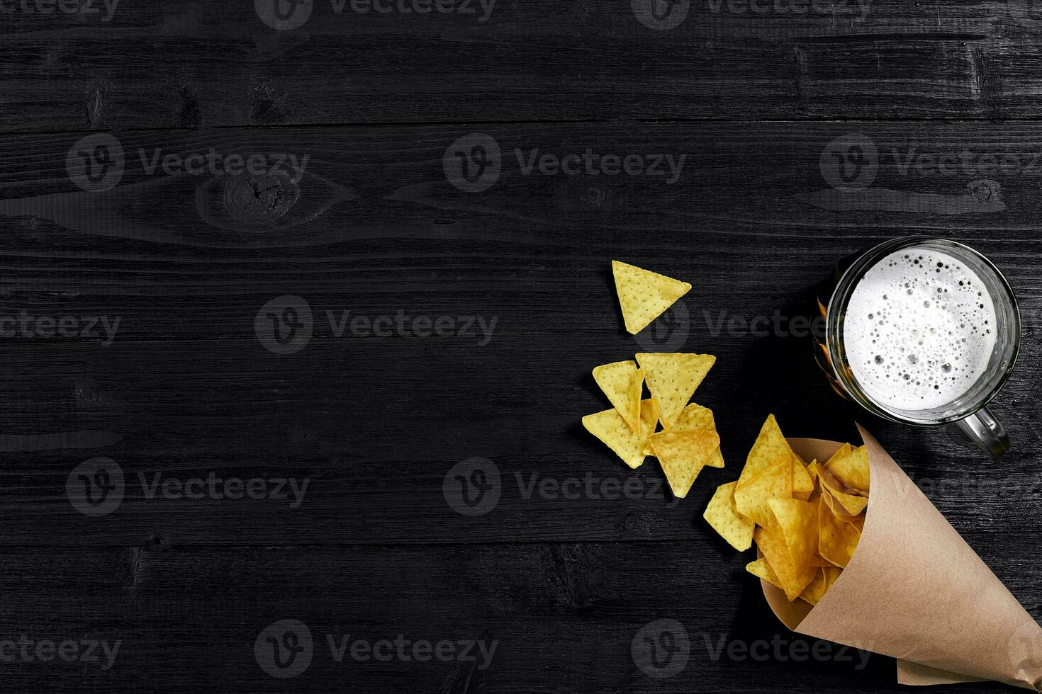 Top view of tortilla chips and glass of beer on black wooden background photo