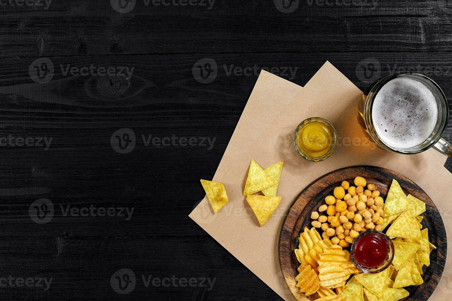 Lager beer and snacks on black wooden table. Nuts, chips. Top view with copyspace photo