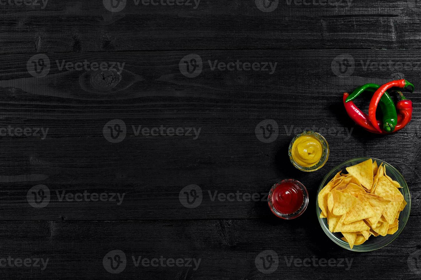 Glass plate with corn chips nachos and tomato sauce on a black wooden table top view. Place for text photo