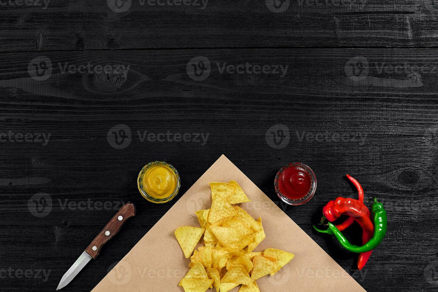 Top view of tortilla chips with sauce and red chili pepper on black wooden background photo