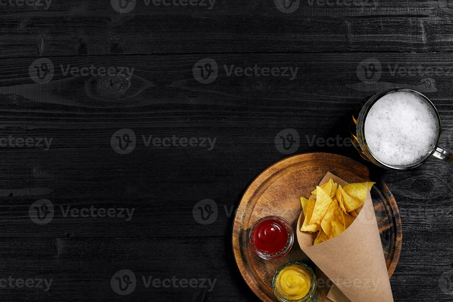 Top view of tortilla chips with sauce, glass of beer on black wooden background photo