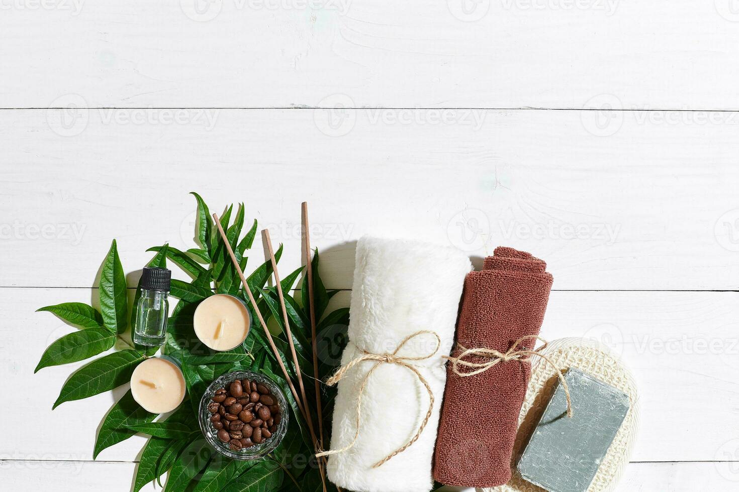Spa set with towel and soap on white wooden background with green leaves photo