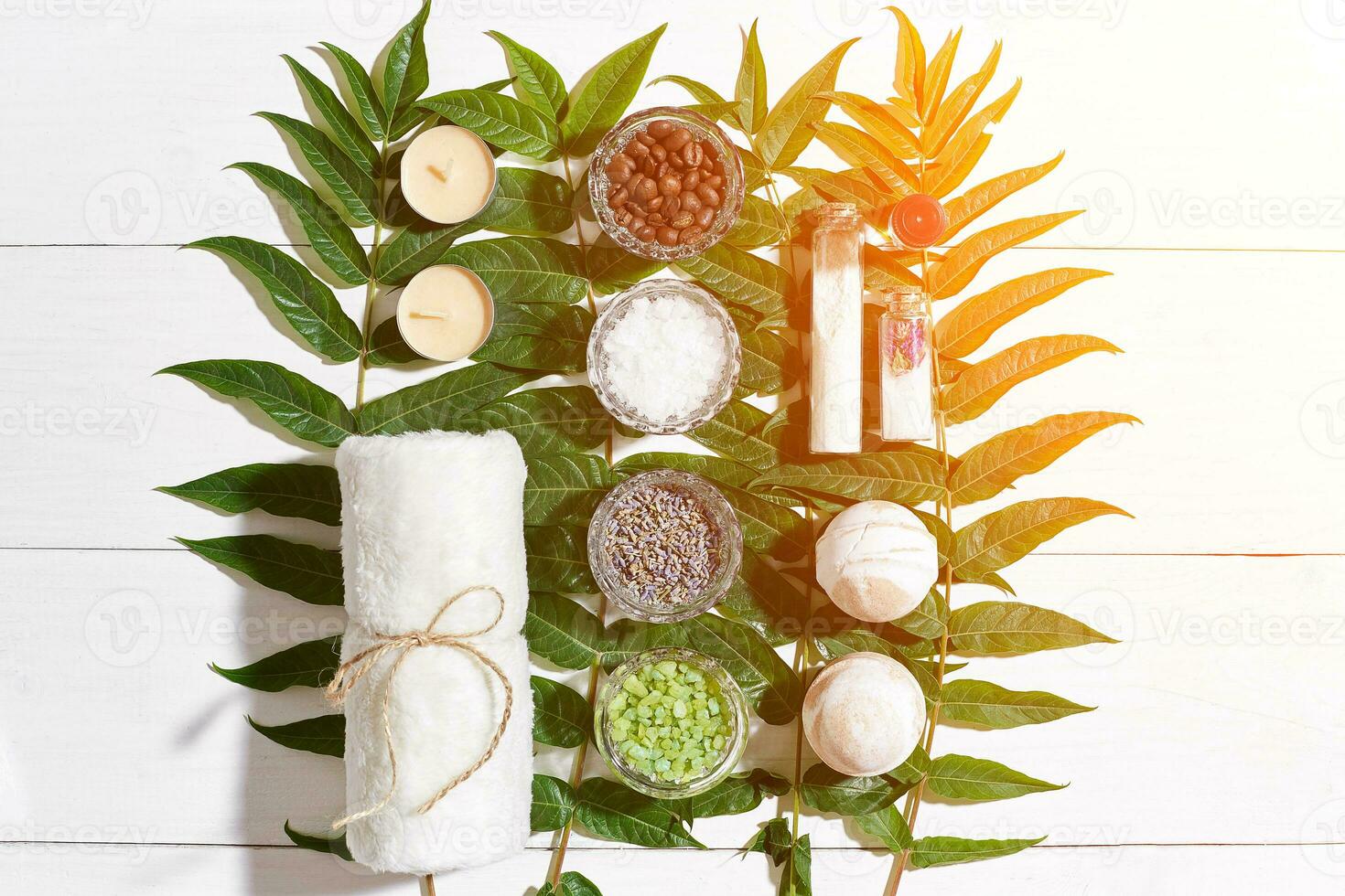 SPA still life with towel, candles, different ingredients for body scrub and green leaves on a white wooden surface. Sun Flare photo