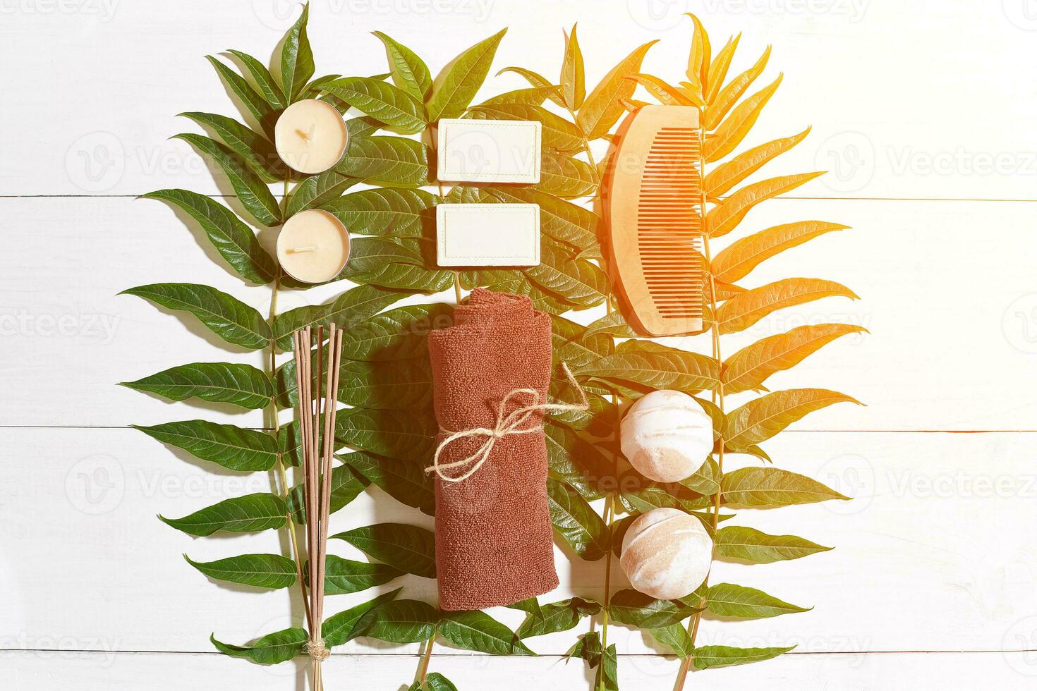 Spa set with towel and soap on white wooden background with green leaves. Sun flare photo